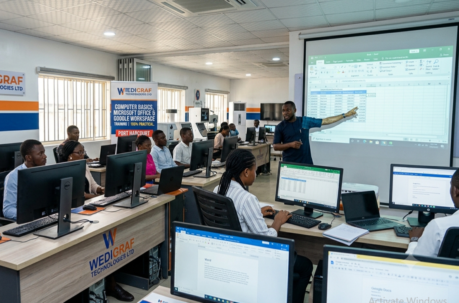 Students and a male instructor inside a modern ICT training center, 100% focused on hands-on practical learning on desktop computers, building an automated Excel financial model at Wedigraf Technologies Ltd in Port Harcourt, Rivers State.